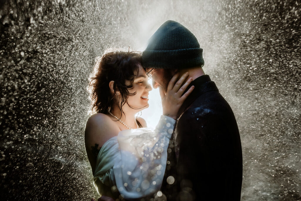 Close-up of Jade and Bradley embracing inside a waterfall cave in South Iceland, with sunlit spray sparkling around them